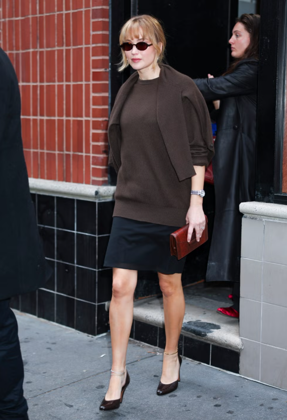 Phong cách minimalism thập niên 90 trở lại mạnh mẽ nhờ Carolyn Bessette Kennedy và phiên bản hiện đại của Jennifer Lawrence. Layer hai chiếc áo cùng tone (một drape nhẹ trên vai) kết hợp chân váy pencil skirt đen, điểm xuyết đồng hồ cổ điển và clutch hoặc túi cầm tay nhỏ mang màu sắc/texture khác nhau, tạo chiều sâu và sự tinh tế cho outfit. Ảnh: Getty Images