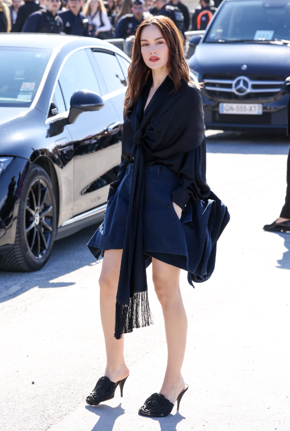 Emilia Schüle diện áo lụa đen mềm rủ, phom suông nhẹ, kết hợp chân váy ngắn cùng tông trung tính. Giày mule cao gót tối giản giúp tổng thể vừa nữ tính vừa sắc sảo, đậm chất street style cao cấp. Ảnh: Getty Images