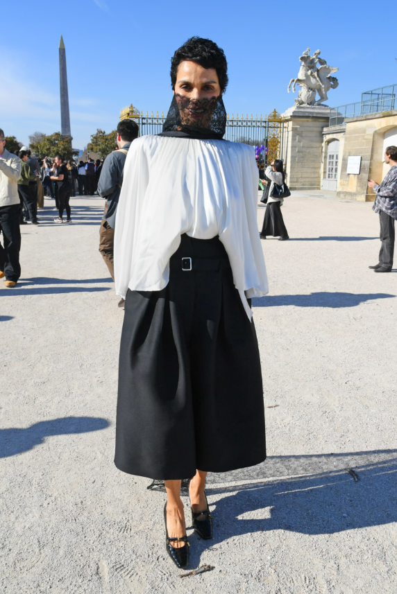 Farida Khelfa diện áo trắng tay phồng phom rộng phối cùng chân váy midi đen thắt lưng bản lớn. Chi tiết ren che mặt tạo hiệu ứng bí ẩn, mang hơi hướng avant-garde và nghệ thuật. Ảnh: Getty Images