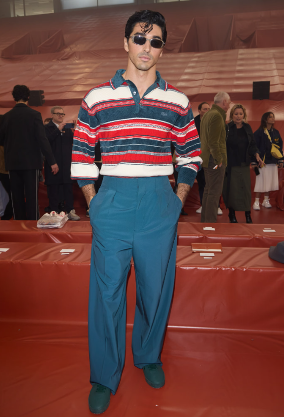 Taylor Zakhar Perez diện áo polo kẻ sọc nhiều màu, phối cùng quần âu dáng suông màu xanh teal. Kính râm là điểm nhấn giúp tổng thể trông hiện đại và cá tính. Ảnh: Getty Images