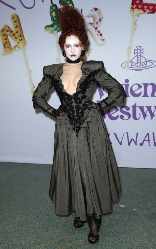 Chappell Roan xuất hiện tại show Thu/Đông 2026 của Vivienne Westwood trong thiết kế váy dạ hội cổ điển với vai phồng và cổ khoét sâu. Chi tiết ren cùng găng tay lưới tạo vẻ huyền bí, độc đáo. Ảnh: Getty Images