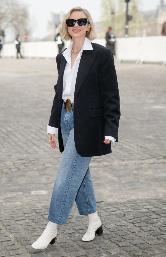 Naomi Watts xuất hiện tại show Thu/Đông 2026 của Celine với phong cách street style thanh lịch: blazer đen oversize phối áo sơ mi trắng và quần jeans ống suông. Cô hoàn thiện diện mạo bằng boots trắng và kính râm bản lớn. Ảnh: Getty Images