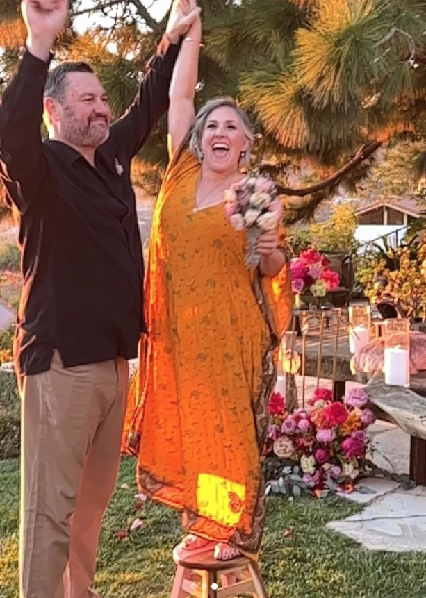 Becca Tobin lựa chọn váy maxi họa tiết màu cam khi tổ chức hôn lễ ngoài trời bên bãi biển cùng Ross Burningham vào đầu năm 2022. Trang phục nhẹ nhàng, rực rỡ hòa hợp hoàn hảo với khung cảnh hoàng hôn trong lễ cưới. Ảnh: Ricki Lake&nbsp;