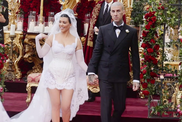 Đám cưới năm 2022 của Kourtney Kardashian và Travis Barker tại Italy cũng từng gây bàn tán mạnh về thời trang. Cô dâu gây ấn tượng với thiết kế mini mang cảm hứng nội y của Dolce & Gabbana, kết hợp khăn voan dài chạm đất thêu họa tiết cùng dòng chữ “family loyalty respect” - trùng với hình xăm trên đầu chú rể. Ảnh: Courtesy of Hulu
