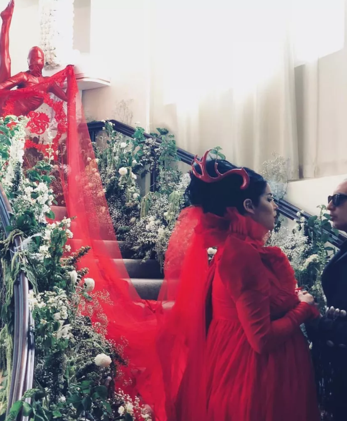 Kat Von D gây choáng ngợp khi từ bỏ váy cưới trắng truyền thống, thay vào đó chọn thiết kế đỏ rực với áo choàng và đuôi dài của Adolfo Sanchez trong lễ cưới lần hai với nhạc sĩ Leafer Seyer. Diện mạo của cô càng thêm ấn tượng với cặp sừng đỏ và phần khăn voan được giữ bởi một người mặc bodysuit cùng tông màu. Ảnh: Kat Von D