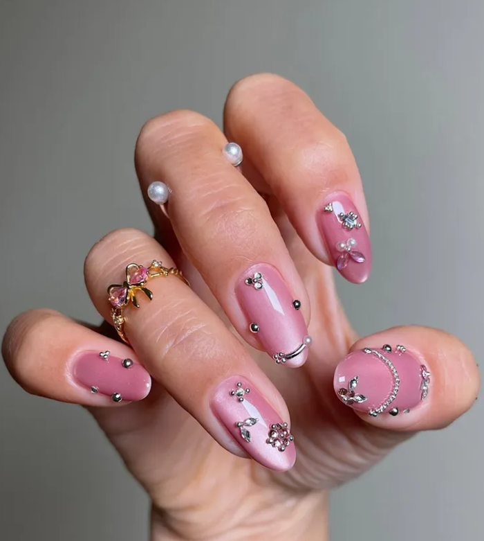 Đối lập là tông hồng kẹo ngọt đang lên ngôi mùa này, với mẫu nail mắt mèo ánh kim kết hợp đính khuyên bạc nhỏ, vừa punk vừa nữ tính. Sự pha trộn giữa nền hồng bubblegum và chi tiết kim loại tạo nên hiệu ứng nổi bật nhưng vẫn giữ được nét mềm mại.