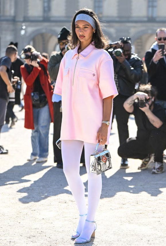 Phong cách vui nhộn với áo polo oversized kết hợp quần tất mỏng. Hoàn thiện bộ cánh bằng túi bạc nổi bật, băng đô và giày cao gót hở mũi, tạo nét hiện đại và sành điệu.