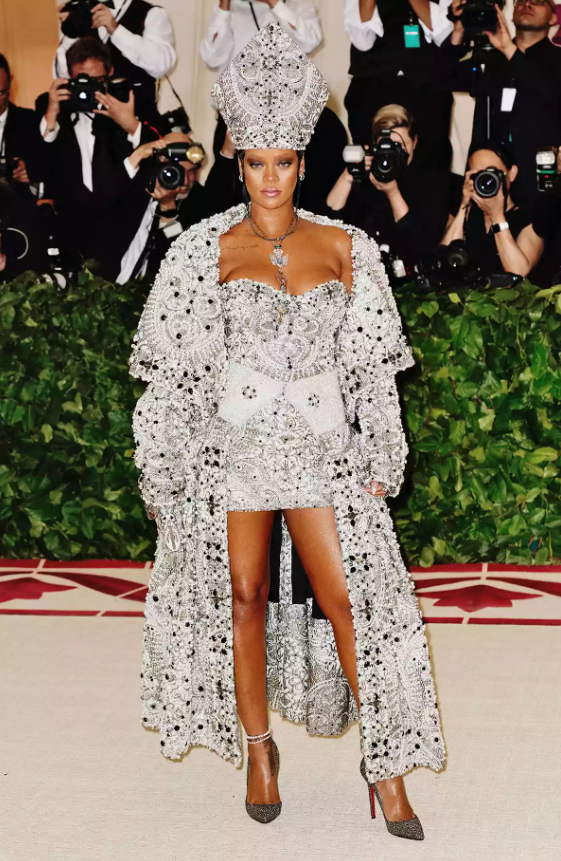 Tại Met Gala 2018 với chủ đề “Heavenly Bodies: Fashion and the Catholic Imagination”, Rihanna gây ấn tượng khi diện thiết kế của Maison Margiela Artisanal, gồm váy mini cầu kỳ kết hợp áo choàng và mũ mitre lấy cảm hứng từ trang phục giám mục. Dù bám sát chủ đề, tạo hình của cô vẫn gây tranh cãi khi một số ý kiến cho rằng hình ảnh này thiếu tôn trọng yếu tố tôn giáo. Ảnh: Getty