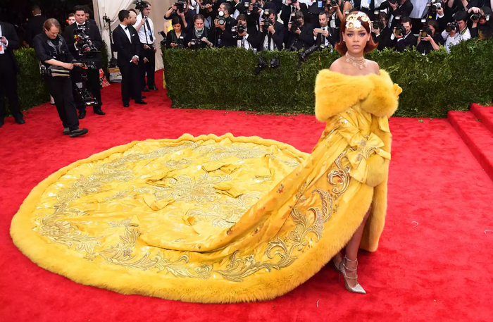 Tại Met Gala 2015, Rihanna gây chấn động với bộ váy vàng viền lông nặng hơn 25 kg do Guo Pei thực hiện, chiếm trọn bậc thềm và trở thành đề tài chế ảnh lan truyền. Nữ ca sĩ sau đó thừa nhận từng lo lắng về phản ứng của công chúng, thậm chí yêu cầu tài xế chạy vòng quanh địa điểm nhiều lần trước khi xuất hiện. Thiết kế cũng vấp phải chỉ trích từ các tổ chức bảo vệ động vật vì sử dụng lông thú. Ảnh: Getty