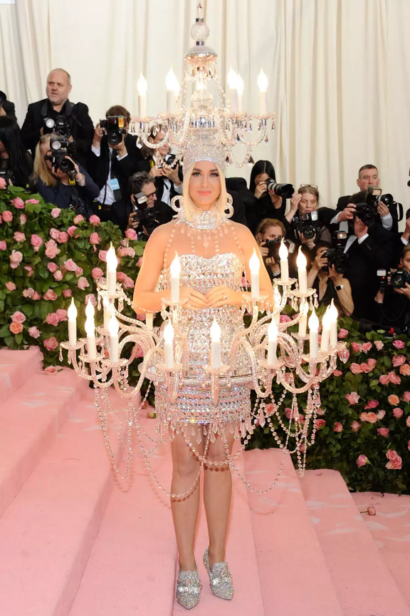 Tại Met Gala 2019, Katy Perry gây chú ý khi hóa thân thành đèn chùm với bóng đèn phát sáng, do Jeremy Scott thiết kế cho Moschino. Trang phục đính pha lê cầu kỳ bám sát chủ đề “Camp”, trước khi cô đổi sang bộ đồ hình hamburger tại sự kiện. Ảnh: WireImage