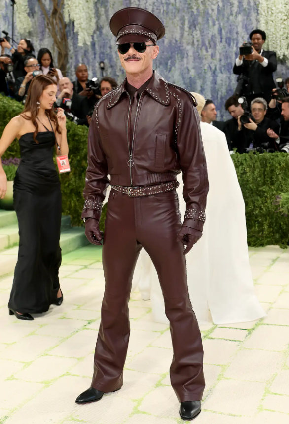 Luke Evans đã bày tỏ lòng kính trọng đối với Tom of Finland bằng bộ trang phục Palomo Spain toàn bằng da với áo khoác, quần và quả địa cầu màu đỏ tía. Chiếc mũ ton sur ton được thiết kế với sự hợp tác của nhà thiết kế mũ người Tây Ban Nha Vivas Carrión. Ảnh: Getty