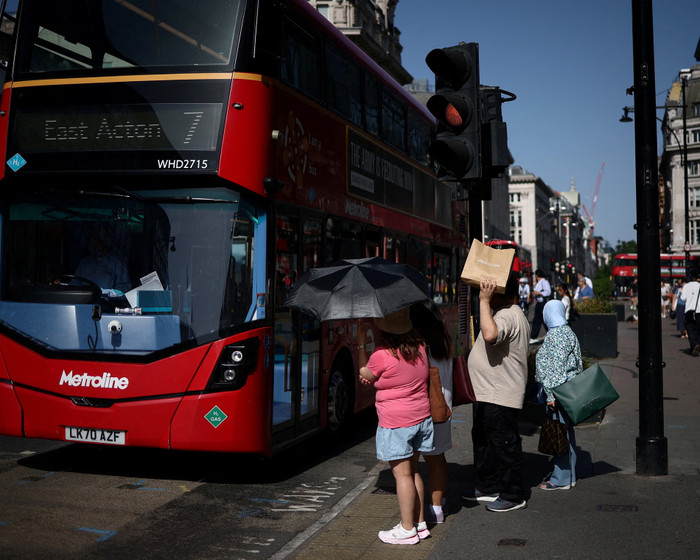 Mọi người dùng ô và túi mua sắm để che nắng trong khi chờ qua đường Oxford.Ảnh: Guglielmo Mangiapane/ReutersPhotograph: Guglielmo Mangiapane/Reuters