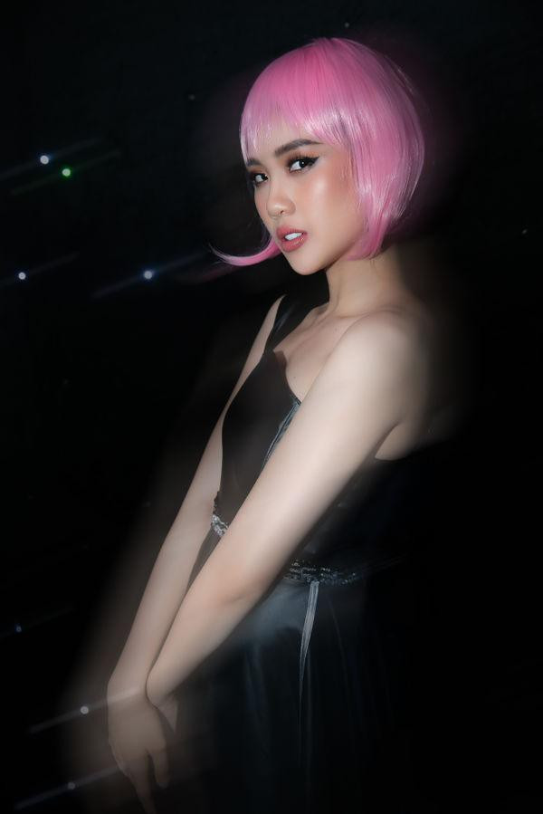 Cô diện mẫu đầm lệch vai, chất liệu da bóng, đội tóc giả gam màu hồng cá tính.