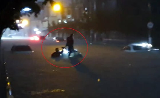 Một người dân phải trèo lên nóc xe để tránh bị chìm trong nước.