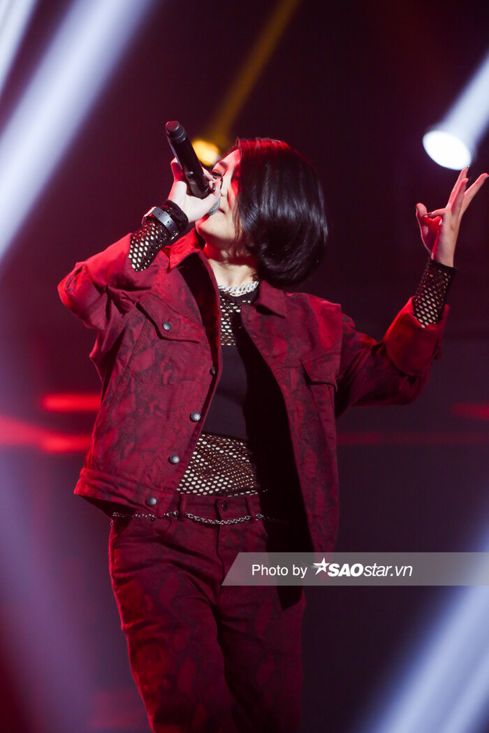 Trên sân khấu, nữ rapper cá tính chọn cho mình set đồ màu đỏ burgundy với jacket và quần xuyệt tông, bên trong là áo lưới đen mix phụ kiện trang sức từ dây chuyền, đồng hồ, thắt lưng xích cùng boots đen 