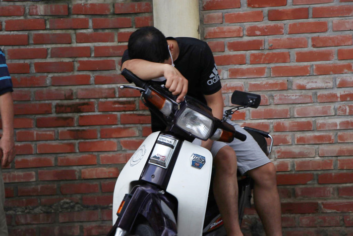 Một phụ huynh đợi con ngoài cổng trường với dáng vẻ mệt mỏi