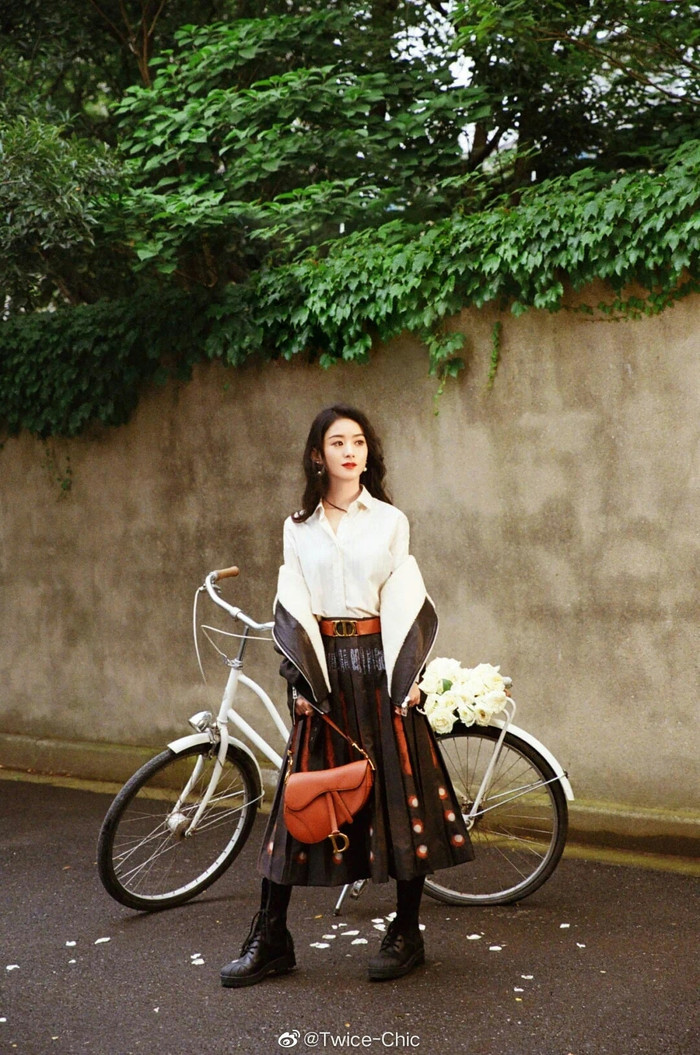 Trang phục đậm mùa thu với kiểu váy chân dài xếp lý, áo sơ mi trắng đi kèm giày đen và kiểu túi màu nâu da bò saddle Dior đình đám khoác hờ jacket bên ngoài 