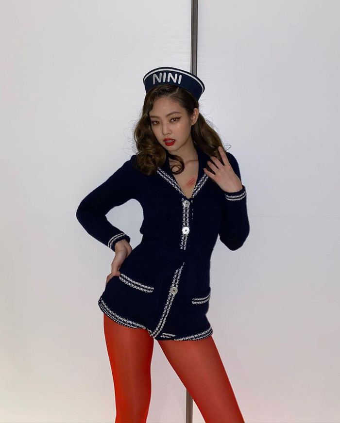 Nữ idol chọn vớ dài màu đỏ mix cùng cả set bodysuit vải tweed cùng kiểu tóc uốn xoăn lọn to và mũ đội đầu với dòng chữ NiNi