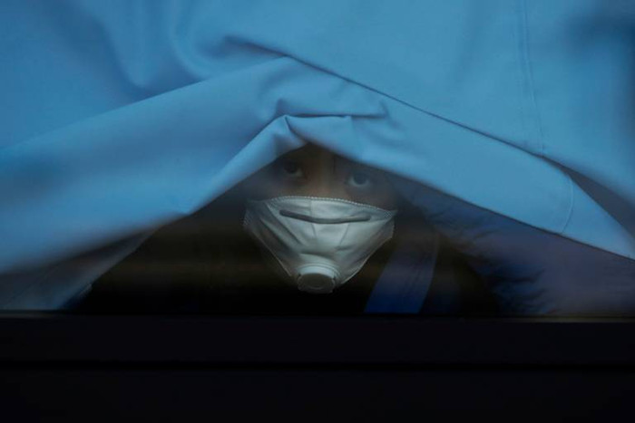 Một hành khách trên du thuyền Diamond Princess vén rèm cửa sổ xe bus nhìn ra ngoài. Sau thời gian cách ly dài đằng đẵng, người này đã được rời khỏi con tàu neo ở thành phố Yokohama, gần thủ đô Tokyo (Nhật Bản) hôm 19/2.