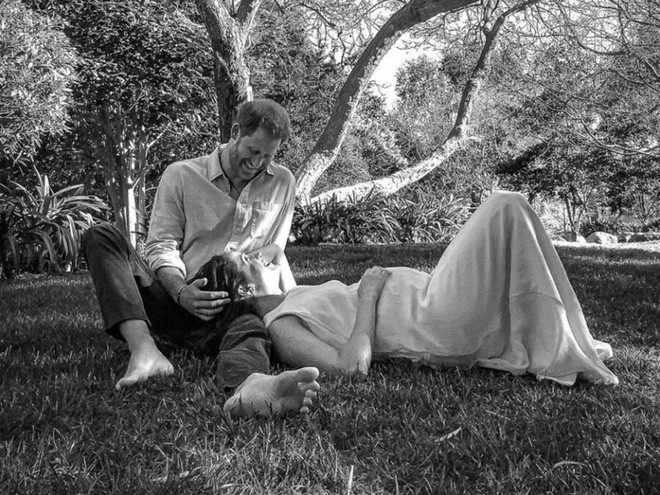 Trong ảnh, cả Harry và Meghan Markle đặt tay lên bụng bầu nở nụ cười hạnh phúc nhìn nhau trìu mến