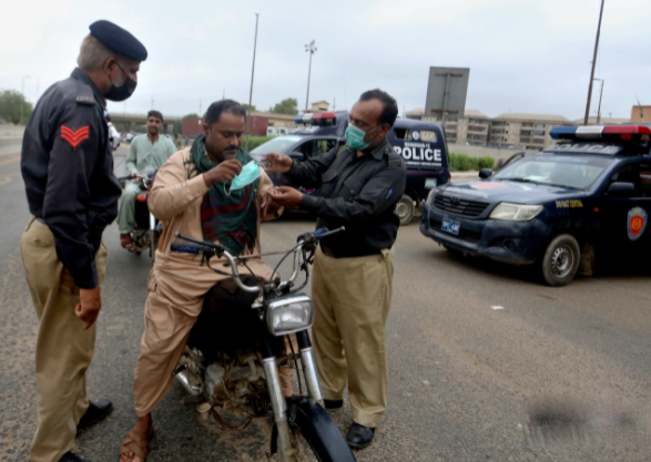 Một sĩ quan cảnh sát giải thích cách đeo khẩu trang đúng cách cho người dân lái xe máy tại một trạm kiểm soát ở Karachi, Pakistan, ngày 31/7.