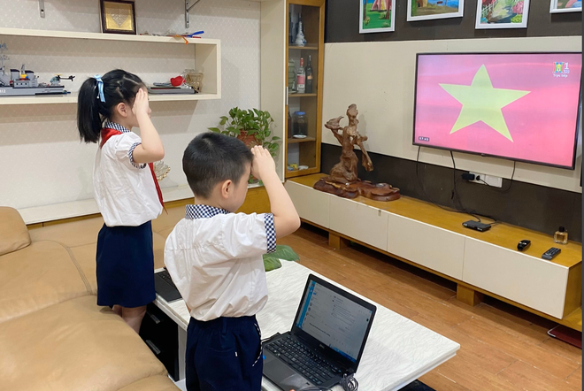 Hai học sinh Hà Nội thực hiện nghi thức chào cờ trong buổi khai giảng qua truyền hình. Nguồn: Dân Trí