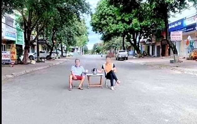 Hai người đàn ông không đeo khẩu trang, màn bàn trà, ghế ra đường ngồi chụp ảnh. Ảnh: BVPL