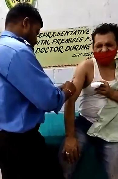 Người đàn ông nhăn mặt, tỏ vẻ đau đớn khi được nam bảo vệ tiêm thuốc. 