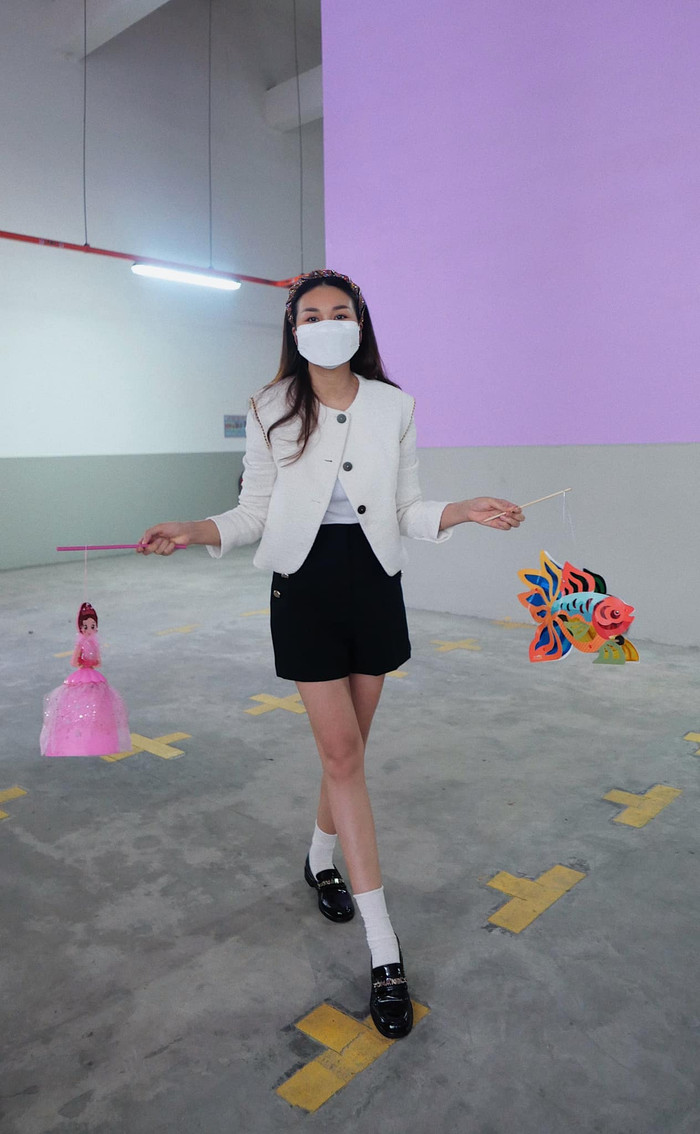 Người đẹp mặc áo blazer trắng mix cùng chân váy đeo phối cùng với trắng, giày âu, hai tay cầm cái lồng đèn