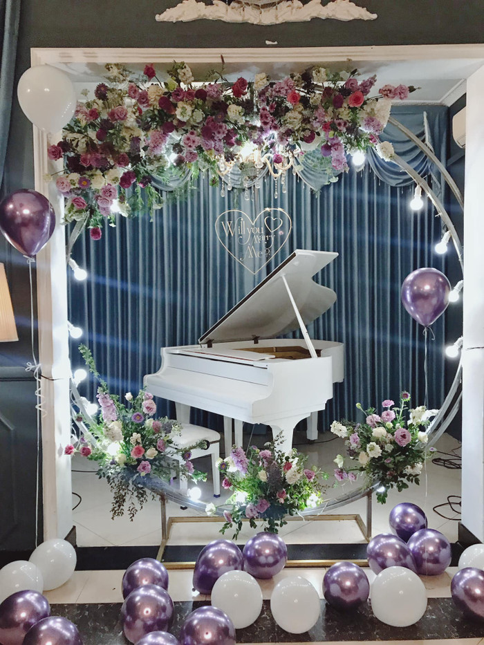 Khung cảnh cầu hôn của cặp đôi được trang trí với màu trắng và tím làm chủ đạo cùng với đó là cây đàn dương cầm.