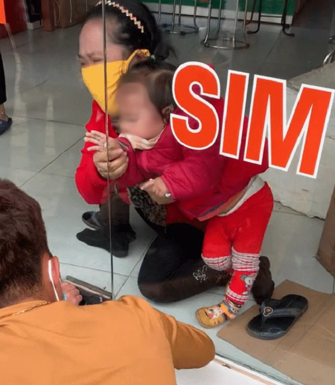 Hình ảnh cháu bé bị kẹt tay vào khe cửa kính của cửa hàng sim thẻ (Ảnh từ Clip)