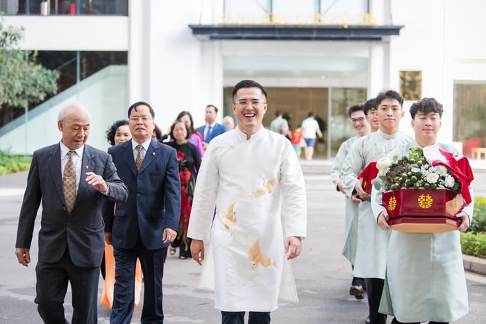 Chú rể Phú Đạt diện áo dài trắng thêu chỉ vàng đồng điệu với vợ.
