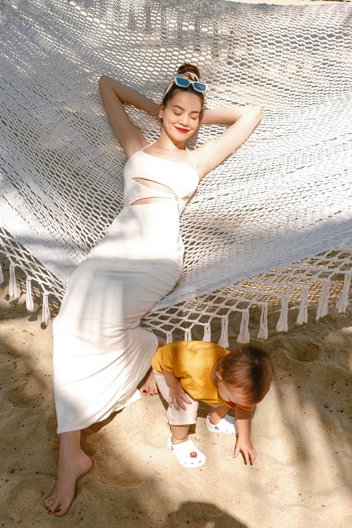 Khi đi chơi cùng các con, Hà Hồ chọn các trang phục đơn giản hơn. Trong một chuyến đi biển cùng gia đình nhỏ, cô chọn một chiếc đầm body trắng đơn giản, có điểm xuyết vài đường cut-out phần eo, kết hợp cùng với mắt kính màu trắng. 
