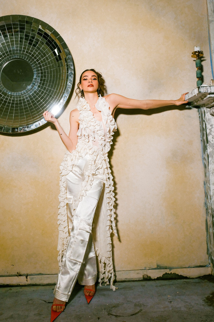 Vốn là một người đa dạng phong cách, Hà Hồ cũng thử với phong cách Y2K quyến rũ, nhắc nhớ về phong cách đầu thập niên 2000. Cô lựa chọn áo đính kết lạ mắt cùng quần lụa trắng dài, nhấn bằng một đôi giày cao gót màu đỏ mũi nhọn ấn tượng.  