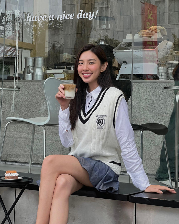 Thùy Tiên 'biến hóa' thành cô sinh viên trong chiếc áo gile viền sọc được thêu kèm logo của trường Đại học. Nàng hậu mix cùng với áo sơ mi trắng và chân váy chữ A để hoàn thiện set đồng phục sinh viên Anh Quốc.