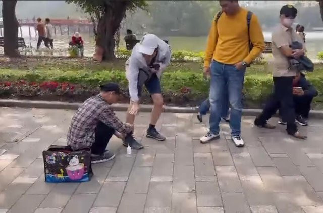 Người đàn ông (áo caro) cố tình chèo kéo khách nước ngoài đánh giày dù người này liên tục xua tay tỏ ý không có nhu cầu. Ảnh cắt từ clip