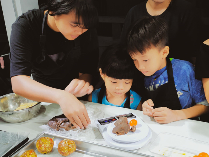 Các em chăm chú nhìn theo hướng dẫn của cô về cách đo khối lượng của nhân bánh